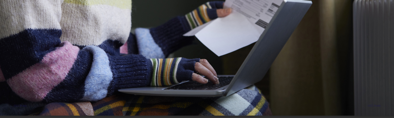 A close-up photo of a person using a laptop while holding an energy bill.